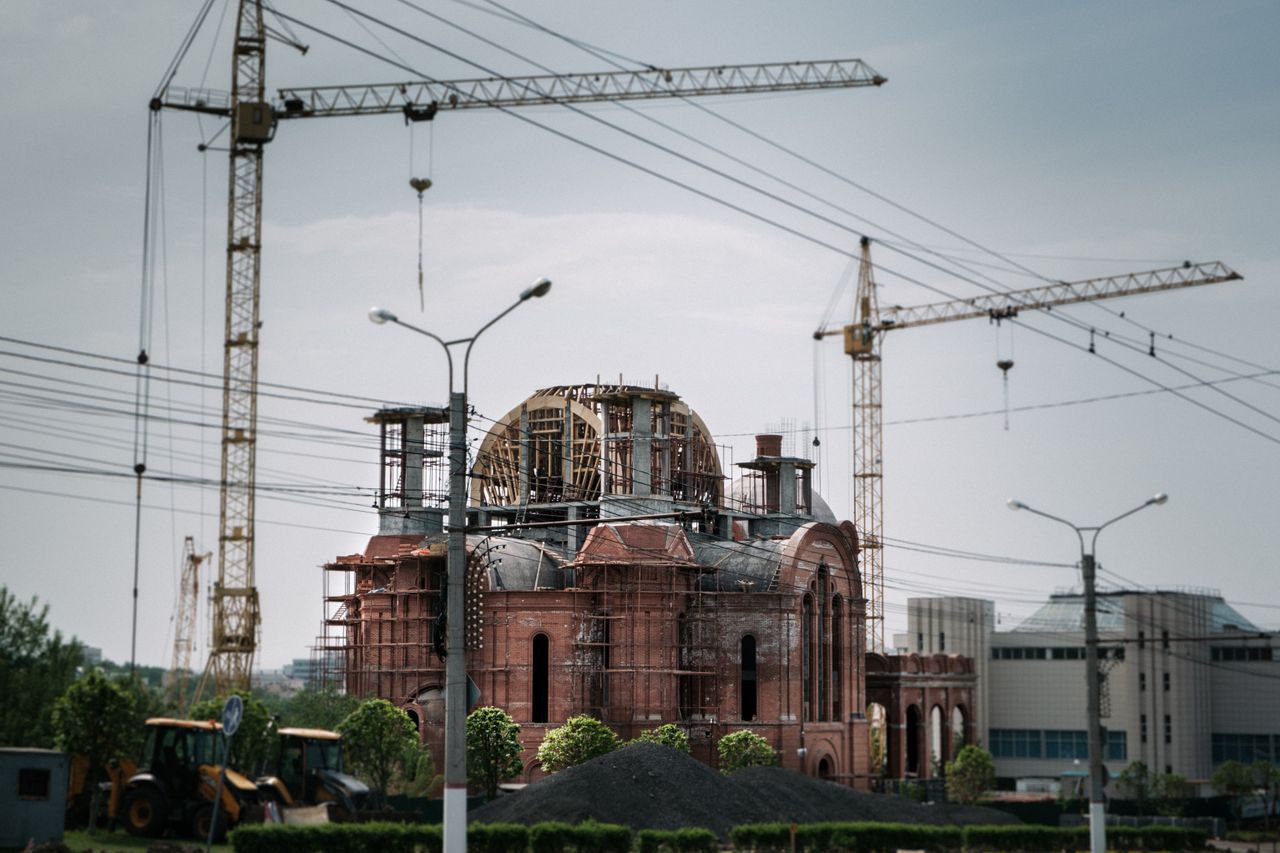 A city scene of a red brick building under construction with visible cranes.